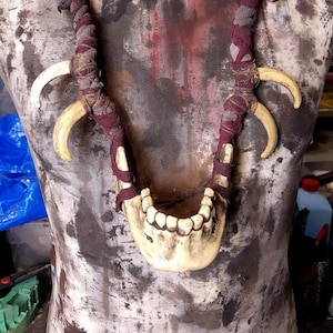 Op de afbeelding: Een ketting gemaakt van bot en stof. De ketting heeft een kaakbeen met tanden, twee bottenklauwen en een gevlochten stoffen koord. De ketting wordt getoond op een mannequin.
