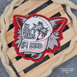 Puede incluir: Pegatina roja y blanca con un lobo de dibujos animados que lleva una gorra de béisbol que dice "In dog years I'm dead".