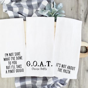 May include: Three white kitchen towels with black text. The first towel says "I'm not sure what I've done to you but I'll take a Pinot Grigio". The second towel says "G.O.A.T. Cheese Balls". The third towel says "It's not about the pasta".