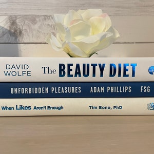 May include: Three hardcover books stacked on top of each other. The top book is white with the title "The Beauty Diet" in blue. The middle book is navy blue with the title "Unforbidden Pleasures". The bottom book is white with the title "When Likes Aren't Enough".