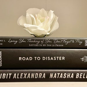 May include: A stack of three black hardback books with white titles. The top book is titled "Loving You, Thinking of You, Don't Forget to Pray: Letters to My Son in Prison" by Jacqueline L. Jackson. The middle book is titled "Road to Disaster" by Brian VanDemark. The bottom book is titled "Exhibit Alexandra Natasha Bell" by Crown.