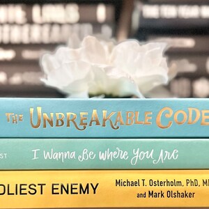 May include: A stack of three books with different colored covers. The top book is blue with gold lettering that reads "The Unbreakable Code". The middle book is green with white lettering that reads "I Wanna Be Where You Are". The bottom book is yellow with black lettering that reads "Deadliest Enemy".
