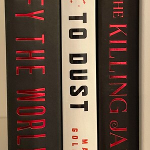 May include: Three hardback books with black covers and red titles. The book on the left is "Defy the Worlds" by Claudia Gray, the middle book is "Gone to Dust" by Matt Goldman, and the book on the right is "The Killing Jar" by Bosworth.