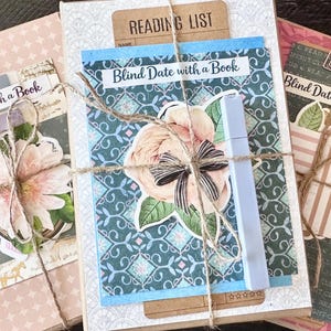 May include: Three wrapped books labeled "Blind Date with a Book" are tied with twine. Each book features decorative paper, floral accents, and a label. One book has a "Reading List" tag. A light blue marker is included.
