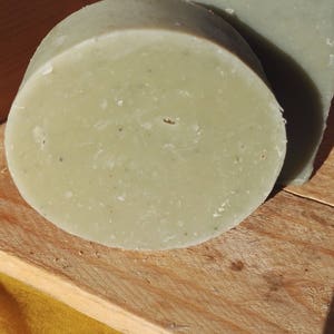 May include: Two bars of green soap on a wooden surface. The soap is round and rectangular in shape.