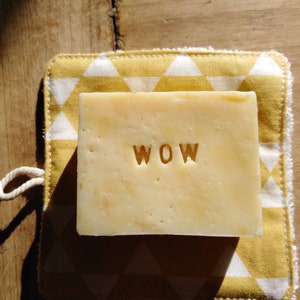 Peut inclure: Un savon avec le mot "WOW" en relief. Le savon est posé sur un tissu à motifs jaunes et blancs.