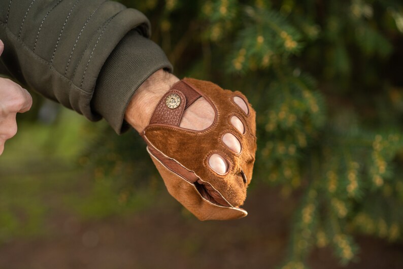 Pu&ograve; includere: Guanti da guida in pelle marrone con fori per le dita e chiusura con bottone in ottone.