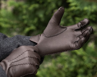 May include: Brown leather gloves with detailed stitching. The gloves are a rich, dark brown color and appear to be made of high-quality leather. The stitching is visible and adds to the gloves' classic design.