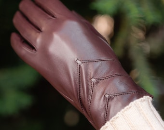 May include: A pair of brown leather gloves with a decorative stitching pattern. The gloves are made of soft, supple leather and have a classic look.
