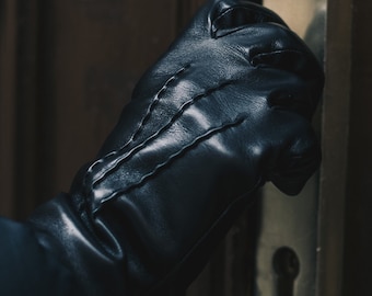 May include: A close-up of a black leather glove with stitching detail. The glove is being used to open a door.