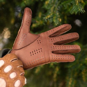 Pu&ograve; includere: Un paio di guanti da guida in pelle marrone con dettagli traforati. I guanti hanno un design senza dita su una mano e un design con dita complete sull'altra.
