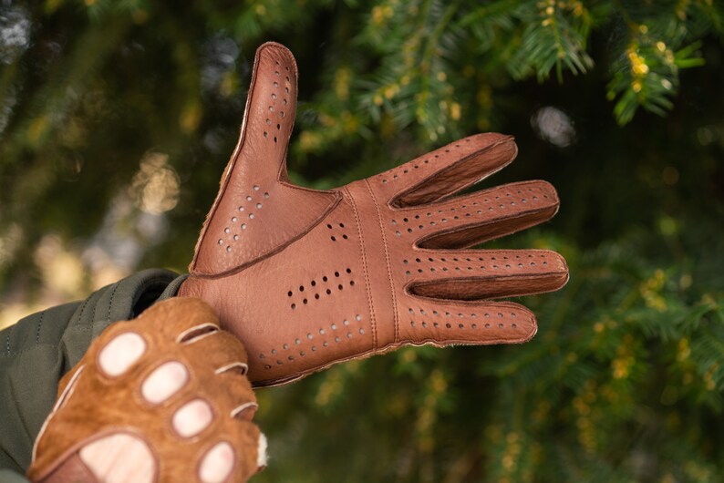 Pu&ograve; includere: Un paio di guanti da guida in pelle marrone con dettagli traforati. I guanti hanno un design senza dita su una mano e un design con dita complete sull'altra.