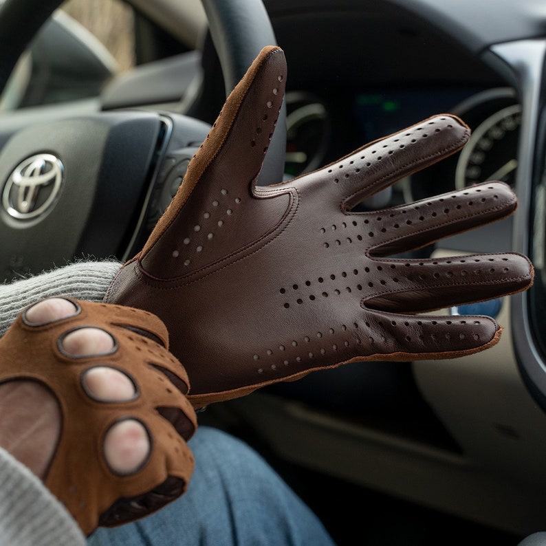 Puede incluir: Un par de guantes de conducir de cuero marr&oacute;n con detalles perforados. Un guante se muestra con los dedos extendidos, mientras que el otro guante est&aacute; parcialmente en la mano de una persona.