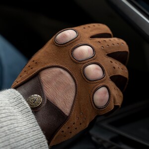 Puede incluir: Guantes de conducir de cuero marr&oacute;n con detalles perforados y una correa de mu&ntilde;eca de cuero marr&oacute;n con un bot&oacute;n de metal. El bot&oacute;n tiene el texto "E.G.A.Z.P. 1969" en &eacute;l.