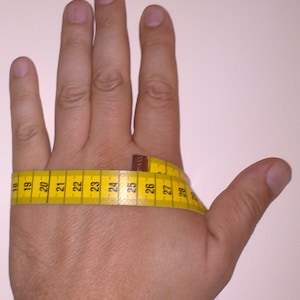 Puede incluir: Una mano con una cinta m&eacute;trica amarilla envuelta alrededor de la mu&ntilde;eca. La cinta lee de 18 a 28 pulgadas. Una segunda cinta m&eacute;trica es visible en el lado derecho de la imagen, con los n&uacute;meros 110 a 113.