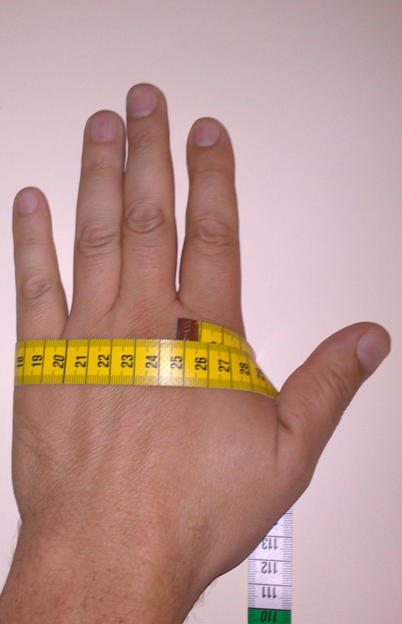 Puede incluir: Una mano con una cinta m&eacute;trica amarilla envuelta alrededor de la mu&ntilde;eca. La cinta lee de 18 a 28 pulgadas. Una segunda cinta m&eacute;trica es visible en el lado derecho de la imagen, con los n&uacute;meros 110 a 113.