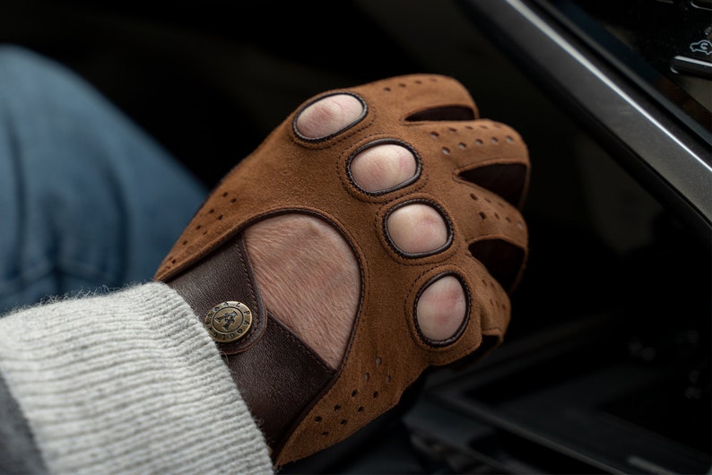 Puede incluir: Guantes de conducir de cuero marr&oacute;n con agujeros para los dedos y una correa de cuero marr&oacute;n con un bot&oacute;n de metal.