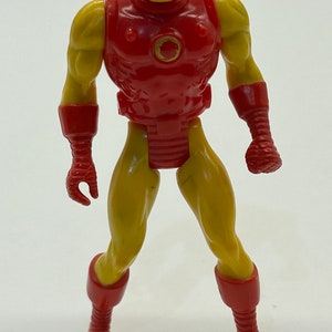 May include: A vintage action figure of Iron Man, with a red and yellow plastic body. The figure has a red chest plate with a circular design and yellow arms and legs.