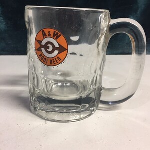 May include: A clear glass mug with a handle. The mug has a logo on the front that says "A&W Root Beer" with an orange and brown circle around the text.