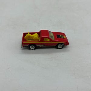 May include: A red toy pickup truck with a yellow motorcycle in the bed. The truck has black tires, a yellow stripe, and the number 22 on the hood. The toy is a miniature replica of a classic vehicle.