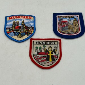 May include: Three embroidered patches featuring Munich landmarks. One patch has a blue border with the text MUNCHEN and a church. Another has a blue border, text MUNCHEN, and city buildings. The third has a red border, text MÜNCHEN, and a figure.