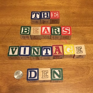 May include: Wooden alphabet blocks spelling out "THE BEARS VINTAGE DEN". The blocks are painted in various colors, including red, blue, green, yellow, and white.