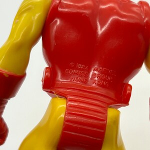 May include: A red and yellow plastic action figure of Iron Man. The figure is standing with its back to the camera. The figure has a copyright notice on the back that reads "&copy; 1984 MARVEL COMICS GROUP HONG KONG."