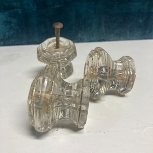 May include: Two clear glass door knobs with a faceted design. One knob has a rusty nail protruding from the top.