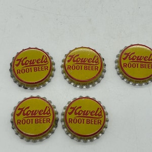 May include: Five vintage Howel's Root Beer bottle caps. Each cap features a yellow center with the brand name and product description in red, surrounded by a silver, crimped edge. The caps are arranged on a light-colored surface.