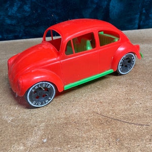 May include: A red toy car with green trim and black wheels. The wheels have the word "AMLOID" printed on them.