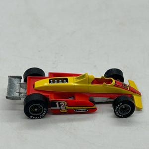May include: A vintage toy race car in red and yellow with black tires. The car features the number 12, Goodyear and Bell branding. The car has a silver rear wing and a detailed engine.