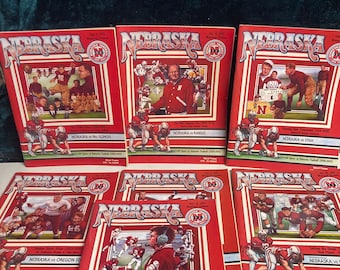 Peut inclure: Une collection de programmes de matchs de football américain vintage des Nebraska Cornhuskers. Les programmes présentent des couleurs rouge et blanche avec des illustrations de joueurs en action. Les programmes datent des années 1970 et 1980 et comprennent des matchs contre le Kansas, l'Illinois, l'Oregon State et l'Oklahoma.