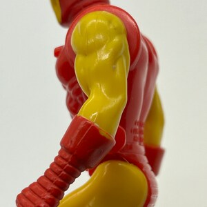 May include: A red and yellow plastic action figure of a superhero. The figure is posed with its right arm raised and its left arm bent at the elbow. The figure has a detailed sculpt and paint job.