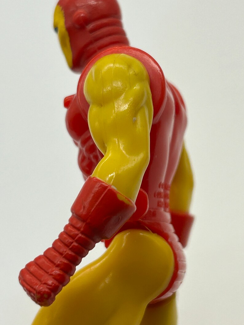 May include: A red and yellow plastic action figure of a superhero. The figure is posed with its right arm raised and its left arm bent at the elbow. The figure has a detailed sculpt and paint job.