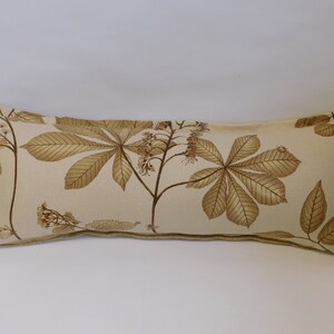 May include: A long, rectangular pillow with a beige background and a brown leaf pattern. The pillow has a subtle texture and a brown trim.