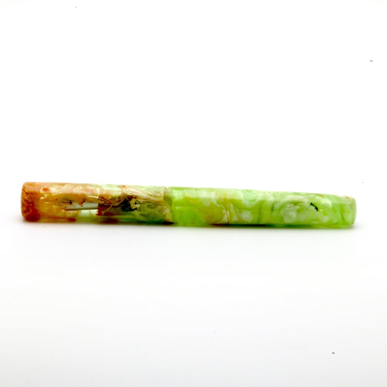 May include: A handcrafted fountain pen with a marbled design. The pen features a vibrant color scheme, with a gradient from orange to green. The pen's body is a mix of green and white, creating a unique aesthetic. The pen is designed for writing.