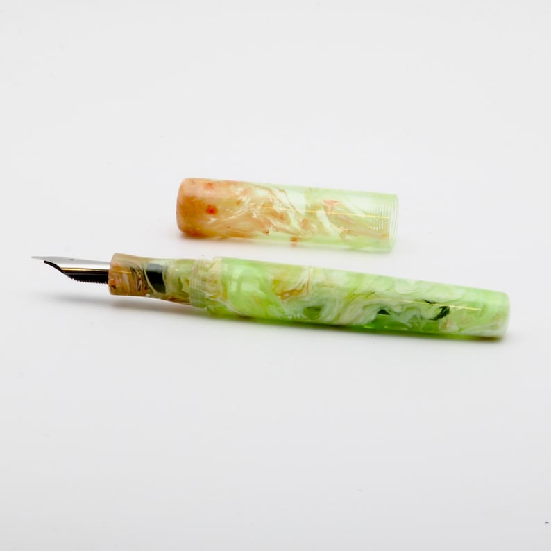 May include: A fountain pen with a marbled design in shades of green, white, and orange. The pen's nib is silver, and the cap is detached, revealing the pen's body. The pen is a writing instrument.