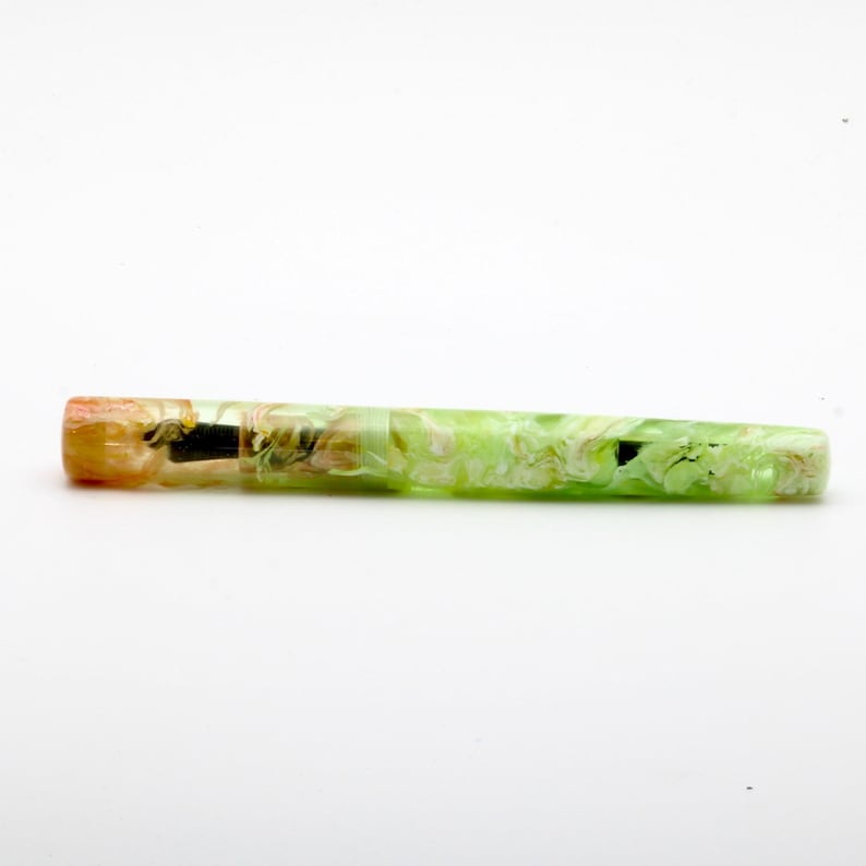 May include: A colorful pen with a marbled design. The pen features a mix of green, yellow, and orange hues. The pen has a gold-colored metal band near the tip.