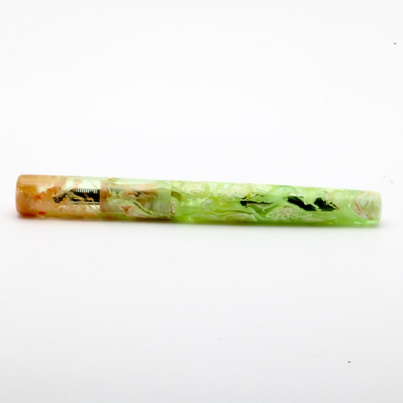 May include: A colorful fountain pen with a marbled design. The pen features a gradient of colors, transitioning from orange to green. The pen's nib is visible, and the overall design is artistic and unique.