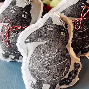 Puede incluir: Primer plano de tres llaveros con forma de cuervo de peluche. Cada llavero presenta un diseño de cuervo en blanco y negro sobre un fondo gris claro, con un borde blanco y esponjoso. Uno está atado con hilo rojo y blanco, y otro tiene un cierre plateado.