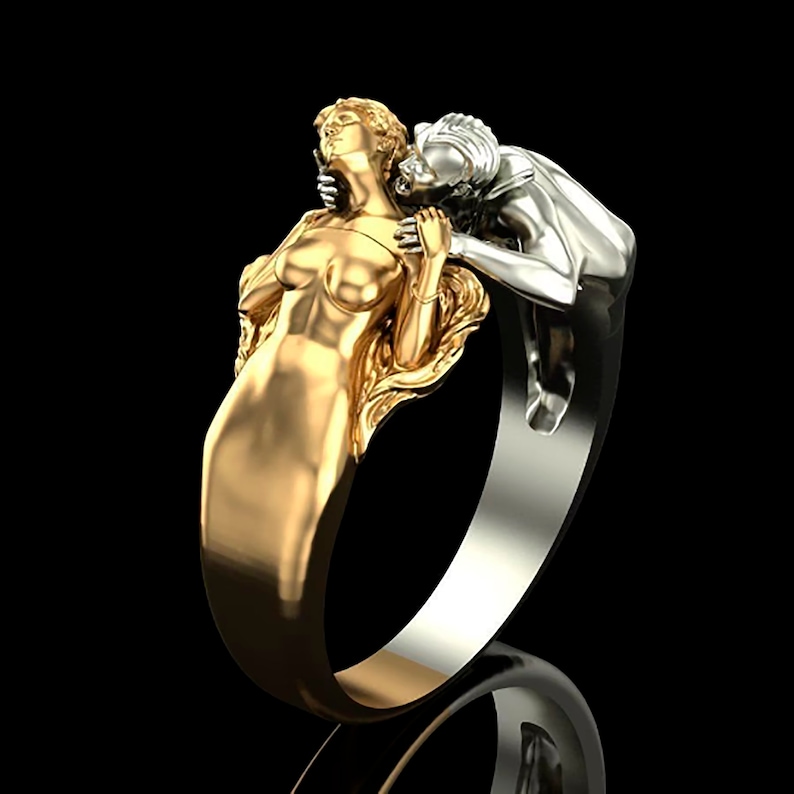 May include: A gold and silver ring featuring a sculpted couple embracing. The woman is gold and the man is silver.