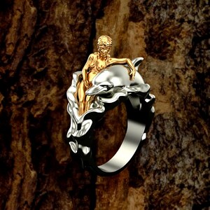 May include: A silver ring with a gold-toned figurine of a woman riding a dolphin. The dolphin is surrounded by stylized waves.