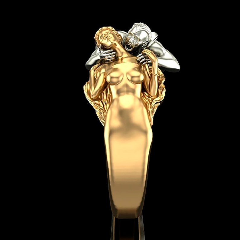 May include: A gold ring featuring a detailed sculpture of a woman being embraced by a man. The woman is wearing a flowing gown and the man is holding her close. The ring is a statement piece with a unique design.