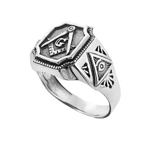 Op de afbeelding: Een zilveren ring met een vrijmetselaars symbool aan de voorkant en een alziend oog ontwerp aan de zijkant.