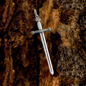 May include: Silver sword pendant with intricate details. The sword has a pointed tip and a cross guard. The pendant is hanging from a chain.