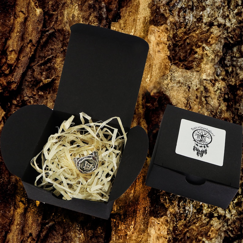 May include: A silver ring with a black and white Masonic symbol in a black gift box with wood shavings. The box has a sticker with a dreamcatcher design and the text "Mystic Jewelry World".