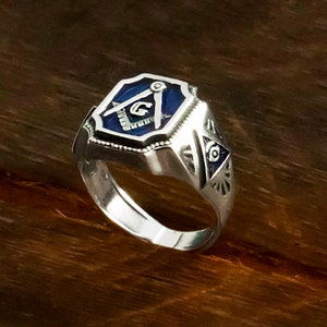 Op de afbeelding: Zilveren vrijmetselaarsring met een blauw ge&euml;mailleerd vierkant en passer ontwerp. De ring heeft ook een alziend oog ontwerp aan de zijkant.