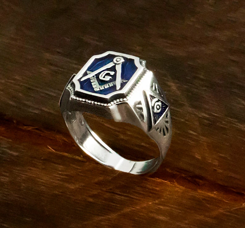 Op de afbeelding: Zilveren vrijmetselaarsring met een blauw ge&euml;mailleerd vierkant en passer ontwerp. De ring heeft ook een alziend oog ontwerp aan de zijkant.
