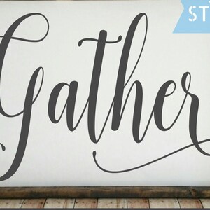 May include: A white wooden sign with the word "Gather" written in black cursive script. The sign is framed with a dark brown wood frame. The word "STENCIL" is written in blue on a white background in the upper right corner of the image.