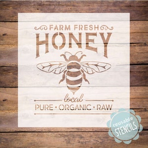 May include: White stencil with the text "Farm Fresh Honey" in a vintage font. A bee illustration is below the text. The text "local" is below the bee, and the text "Pure Organic Raw" is below that. The text "Reusable Stencils" is in a circle at the bottom right corner.